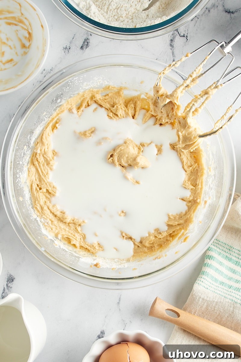 Overhead view of the final portion of buttermilk being poured into the batter in a mixing bowl.