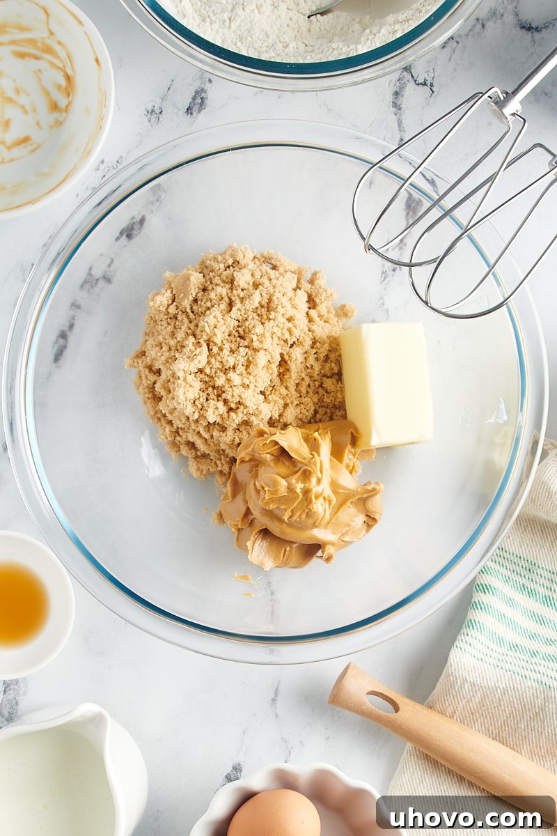 Overhead view of softened butter, light brown sugar, and creamy peanut butter in a glass mixing bowl before beating.