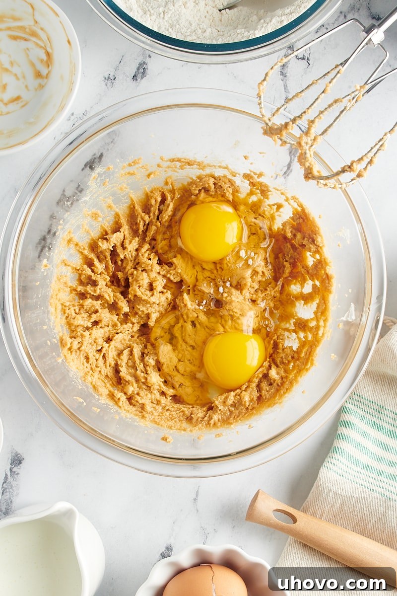 Overhead view of eggs being added to the creamed butter, sugar, and peanut butter mixture in a mixing bowl.