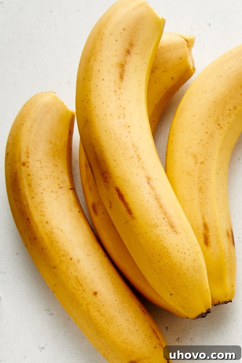 Four perfectly ripe bananas on a white countertop, ready for baking