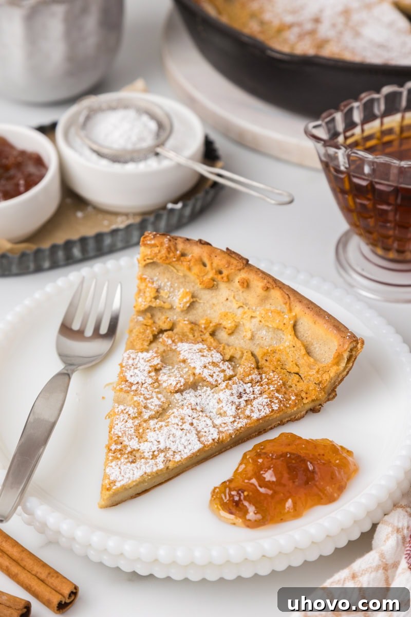 a slice of Dutch baby pancake dusted with powdered sugar and served with a dollop of raspberry jam on a white plate