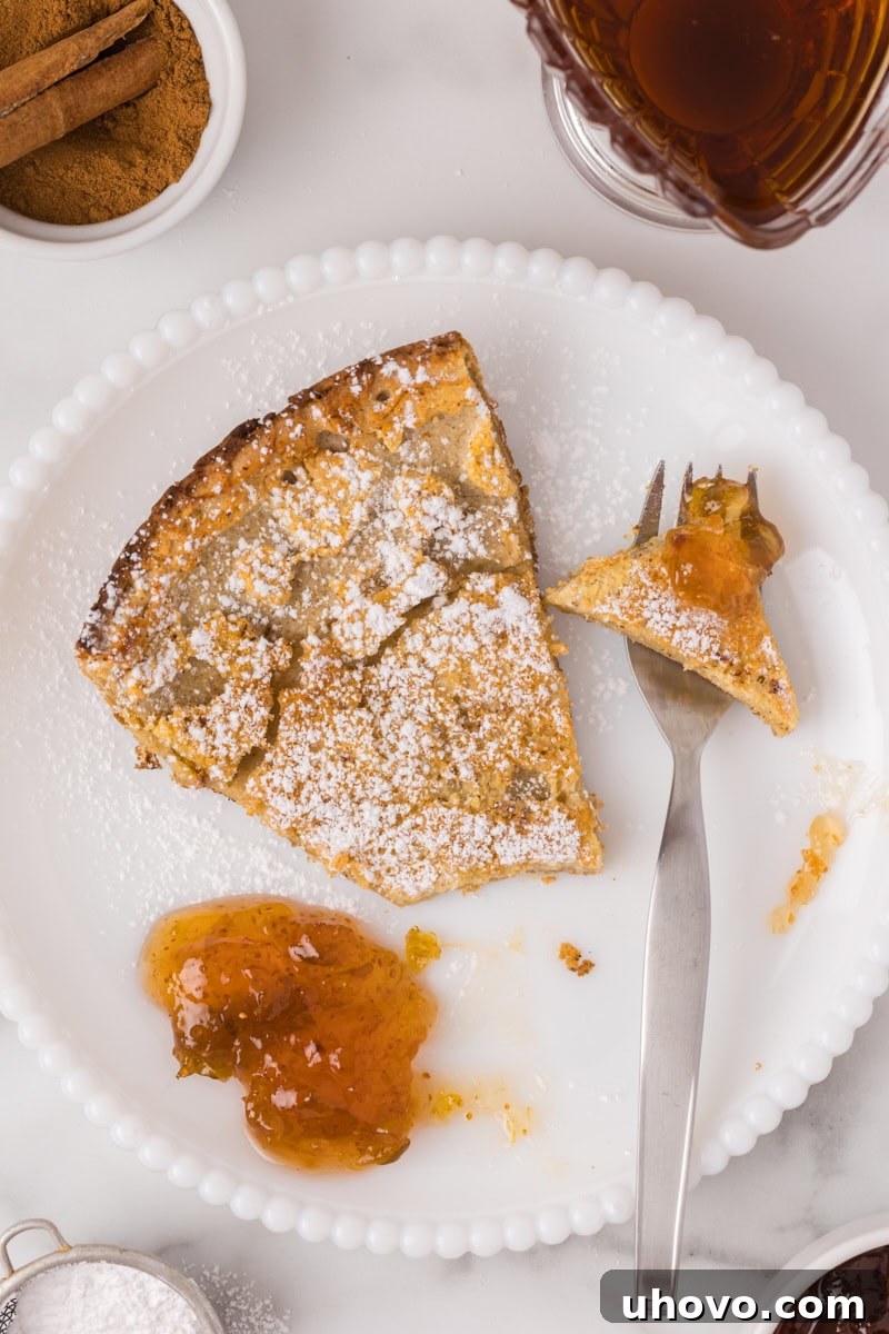 a slice of Dutch baby pancake on a white plate with a bite taken from it, topped with jam, and a fork resting beside it