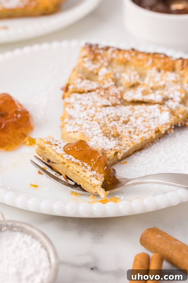 a bite of Dutch baby pancake topped with jam on a fork with the remaining serving of pancake behind it