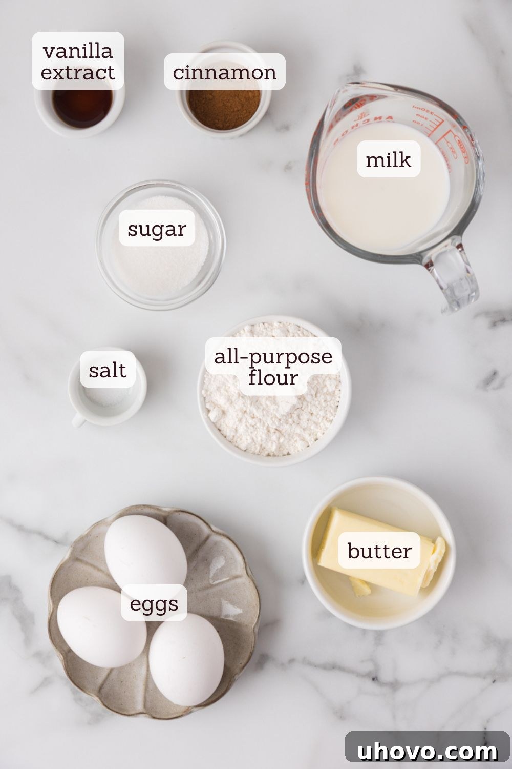 overhead view of key ingredients for making Dutch baby pancake, including eggs, flour, milk, sugar, cinnamon, vanilla extract, and butter