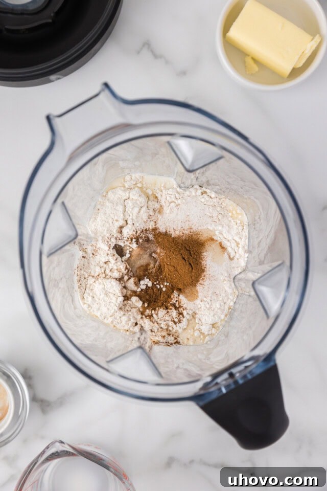 overhead view of eggs, flour, milk, sugar, cinnamon, vanilla, and salt in a blender, ready to be mixed
