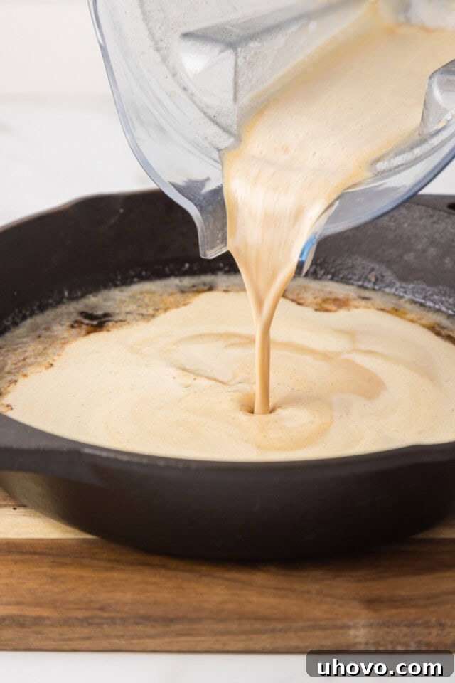 Dutch baby pancake batter being carefully poured into melted butter in a hot cast iron skillet
