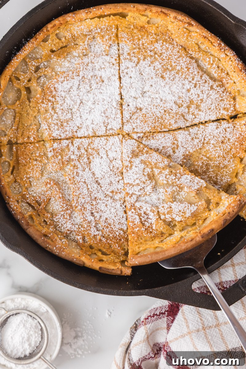 overhead view of a perfect slice of Dutch baby pancake being lifted from the remaining pancake in a cast iron skillet, showcasing its airy texture