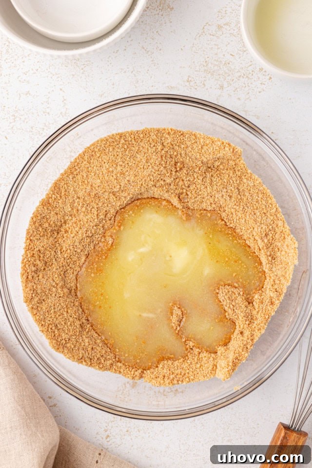 Melted butter being poured into a bowl of graham cracker crumbs and sugar, illustrating the first step of crust preparation.