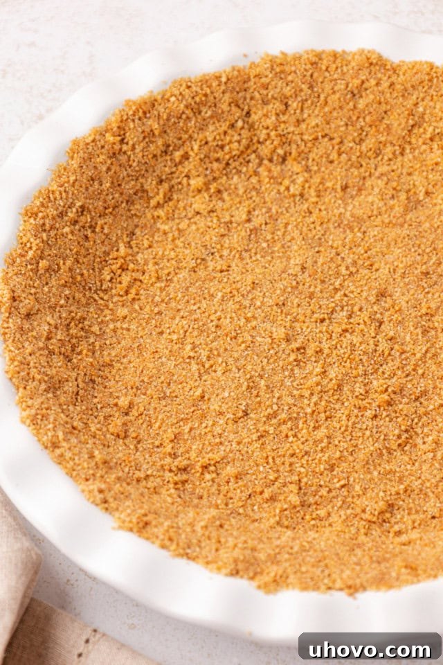 The graham cracker crust firmly pressed into a white ceramic pie plate, forming a neat and even layer.