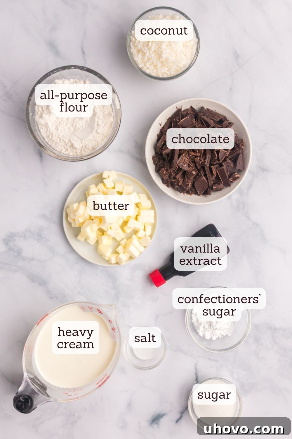 Overhead view of key ingredients for a homemade chocolate mousse pie: dark chocolate chunks, heavy cream, vanilla extract, shredded coconut, and cubes of cold butter.
