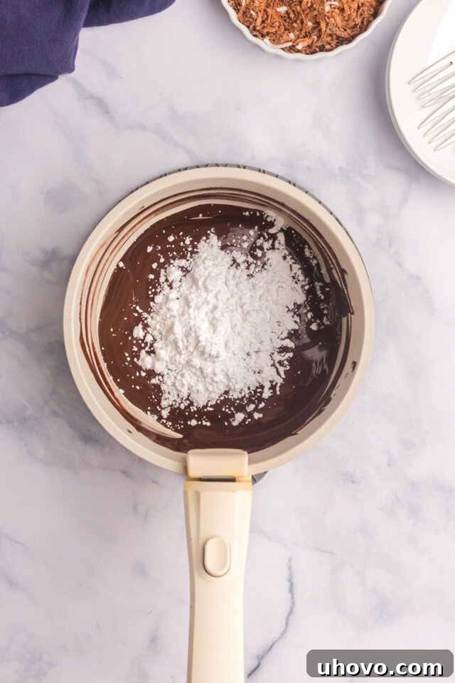 Overhead view of confectioners' sugar and vanilla extract being stirred into a bowl of perfectly melted dark chocolate.