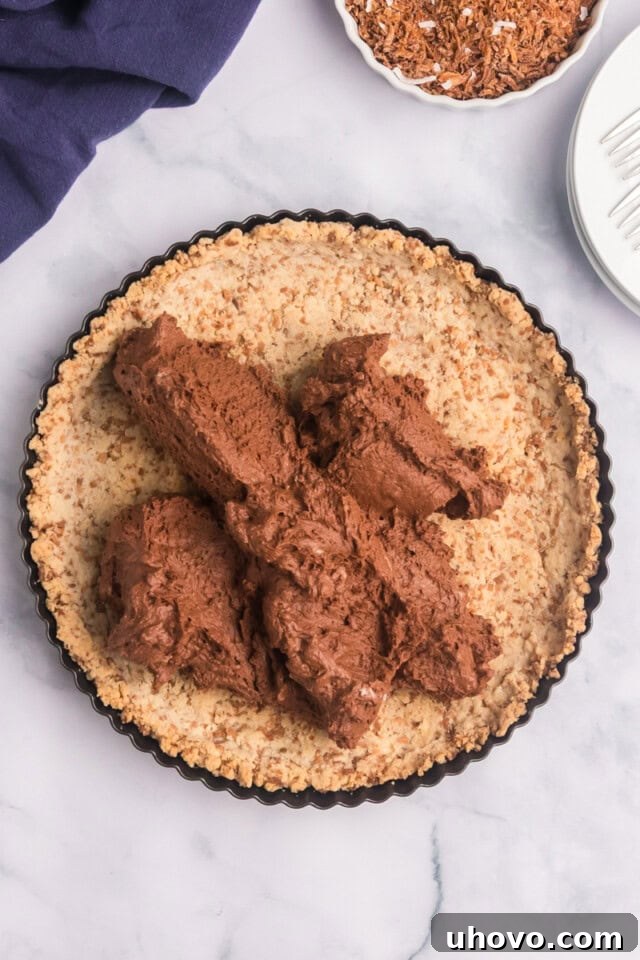 Overhead view of the smooth chocolate mousse filling being evenly spread into a toasted coconut shortbread crust.