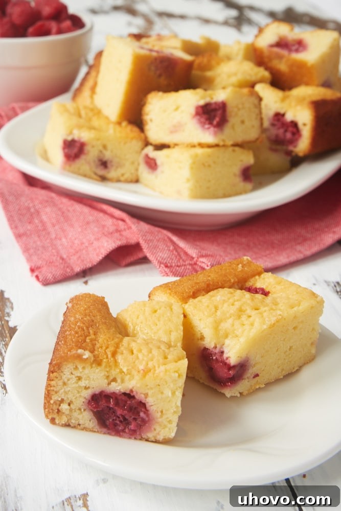 A stack of Raspberry White Chocolate Brownies on a plate, with a close-up showing the soft interior and fresh raspberry pieces.