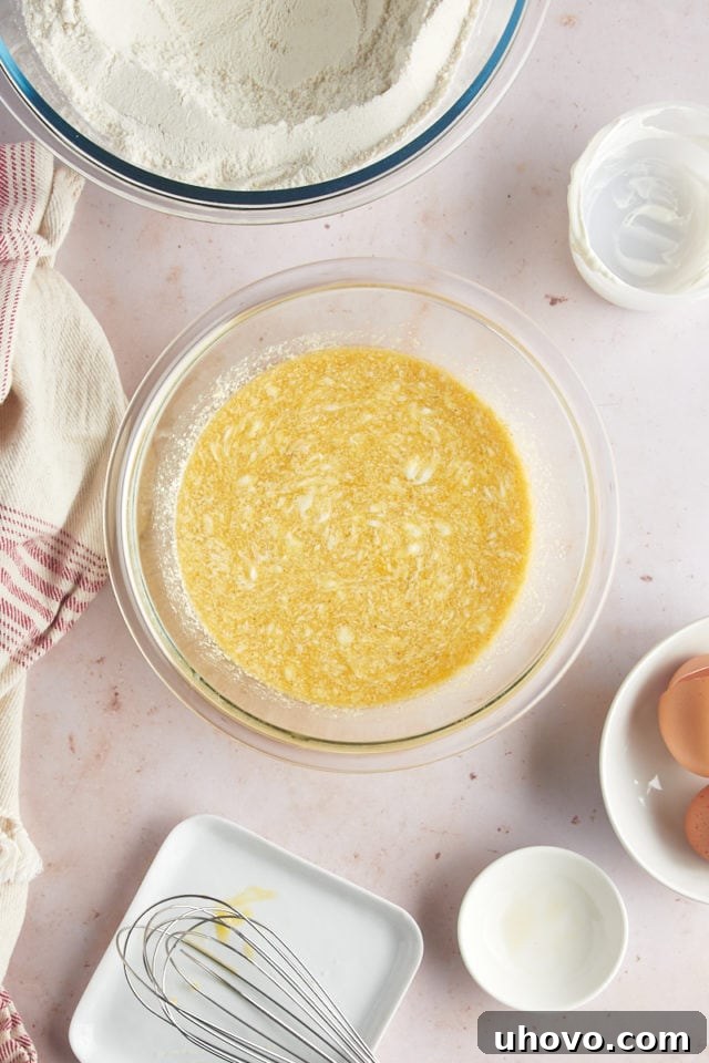 An overhead view of the combined wet ingredients—beaten eggs, brown butter, sour cream, and vanilla extract—perfectly mixed in a glass mixing bowl, ready to be added to the dry ingredients.