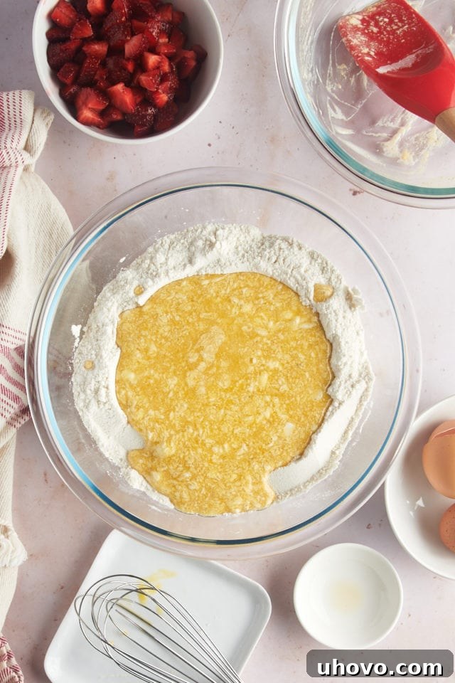 An overhead view of the wet ingredients mixture being carefully poured into the well created in the dry ingredients in a large glass mixing bowl.