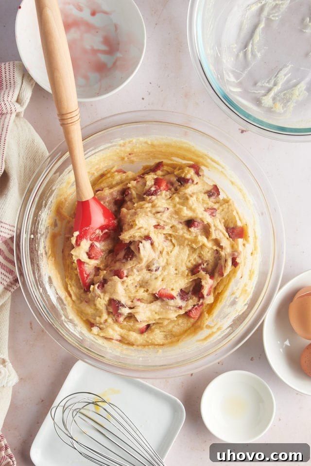 An overhead view of the finished strawberry muffin batter in a glass mixing bowl, perfectly mixed with strawberries evenly distributed, ready for portioning.