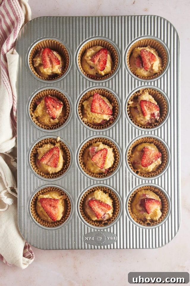 An overhead view of the muffin pan with all strawberry muffins topped with a strawberry slice and a sprinkle of coarse sugar, ready to be placed in the oven.