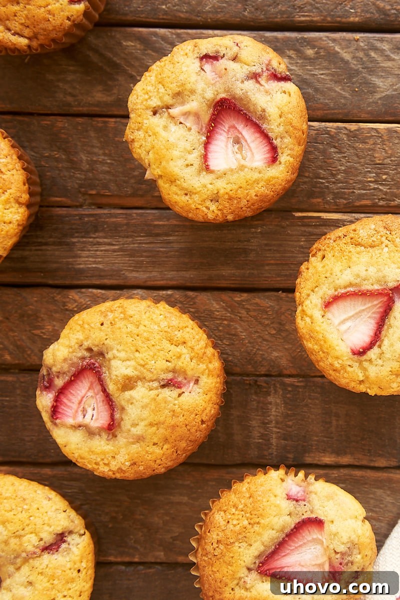 An overhead view of freshly baked brown butter strawberry muffins scattered artfully on a light wooden surface, highlighting their perfectly browned tops and inviting texture.