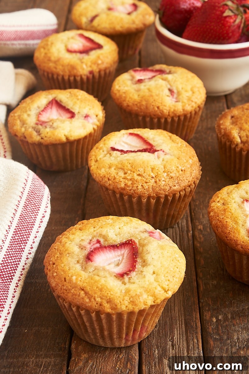 A delightful arrangement of brown butter strawberry muffins beside a small bowl of fresh whole strawberries on a rustic wooden surface, creating a vibrant and inviting scene.