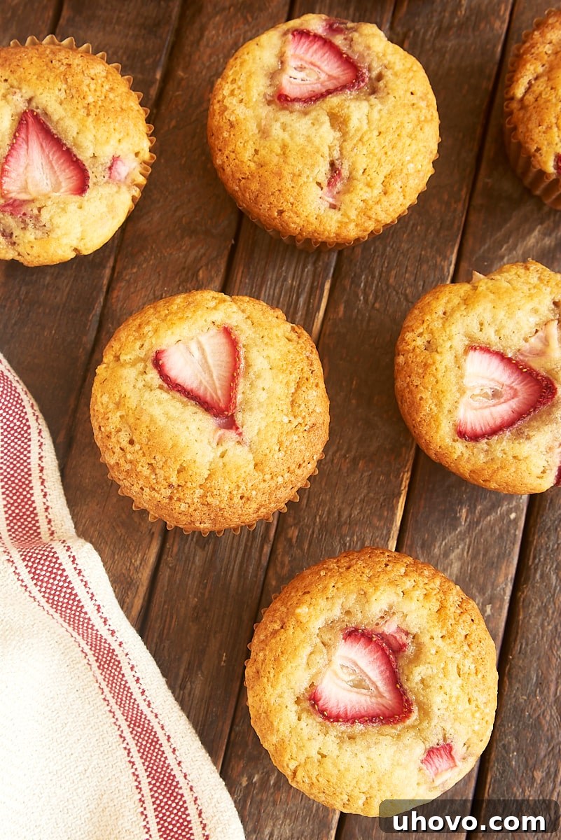 A perfectly arranged row of brown butter strawberry muffins on a wooden surface, showcasing their appealing golden-brown crusts and inviting texture.