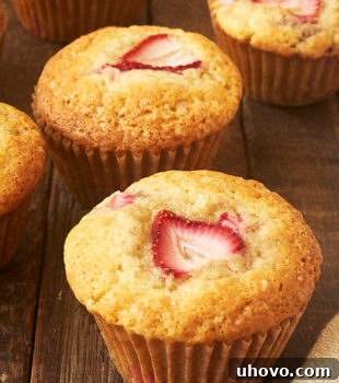 A single strawberry muffin on a wooden surface with more muffins in the background, showcasing its delicious appeal.