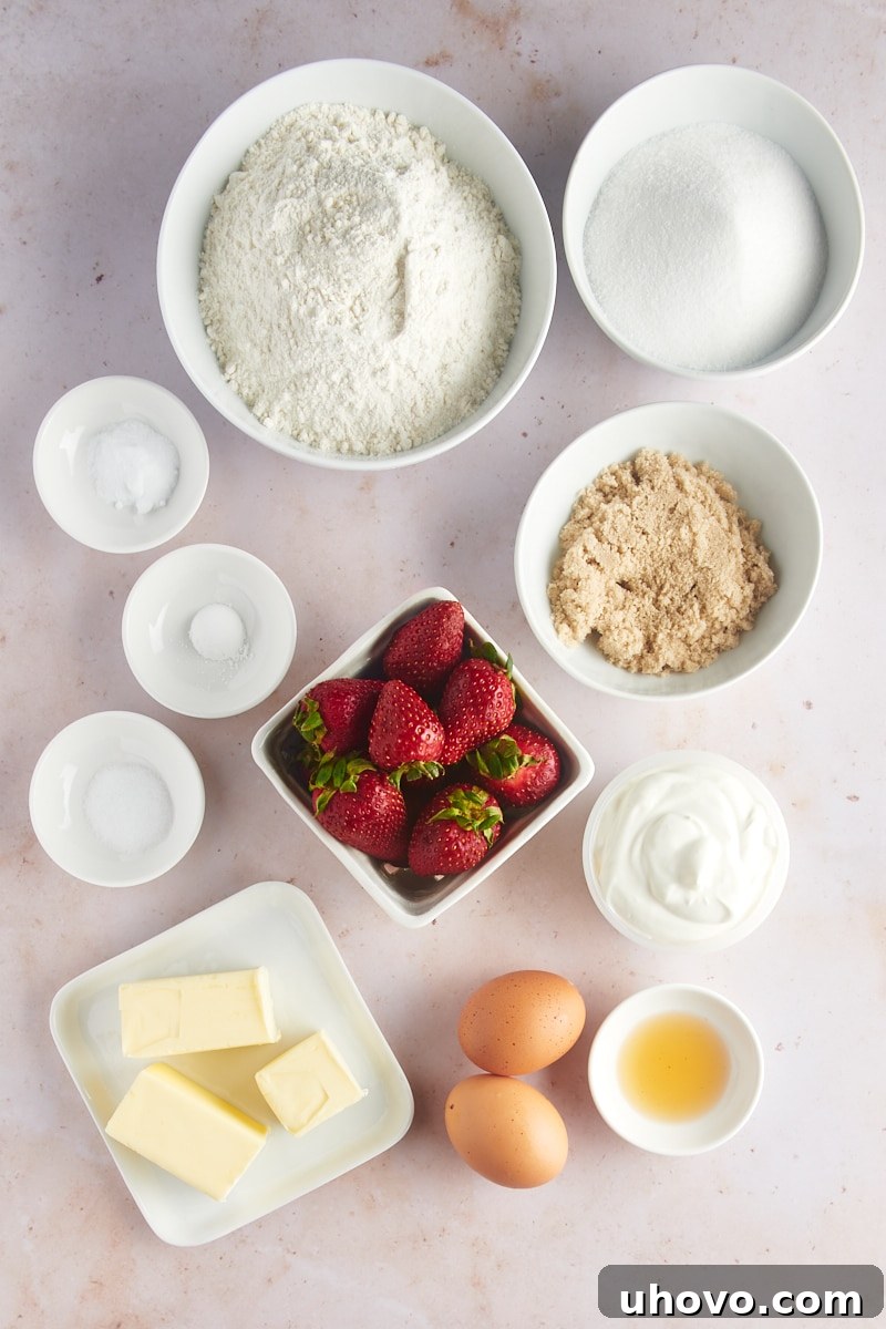 An organized overhead view of all the essential ingredients laid out for making brown butter strawberry muffins, including butter, flour, sugar, eggs, sour cream, and fresh strawberries.