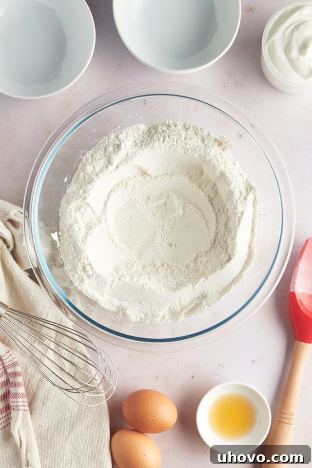 An overhead view of the thoroughly mixed dry ingredients, including both granulated and brown sugars, in a glass mixing bowl, forming a well in the center.