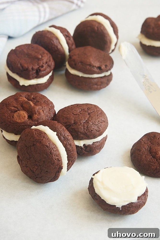 Hands carefully assembling a Brownie Cookie Sandwich, placing a generous dollop of cream cheese frosting onto one cookie before topping it with another.