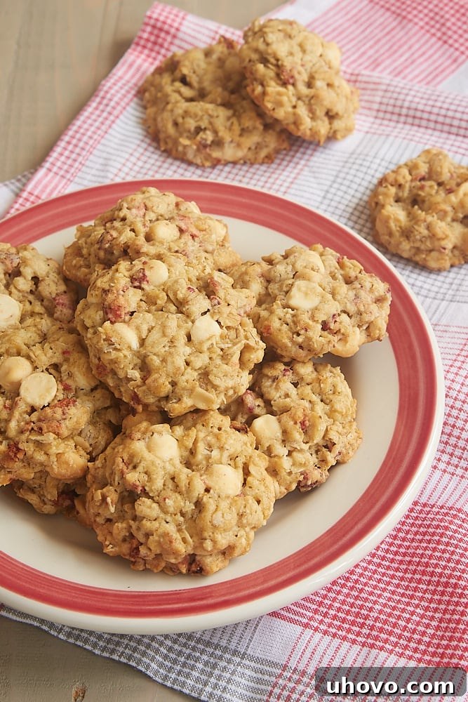 A close-up stack of golden brown Strawberry White Chocolate Oatmeal Cookies on a red-rimmed plate, highlighting their perfectly baked edges and delicious inclusions.