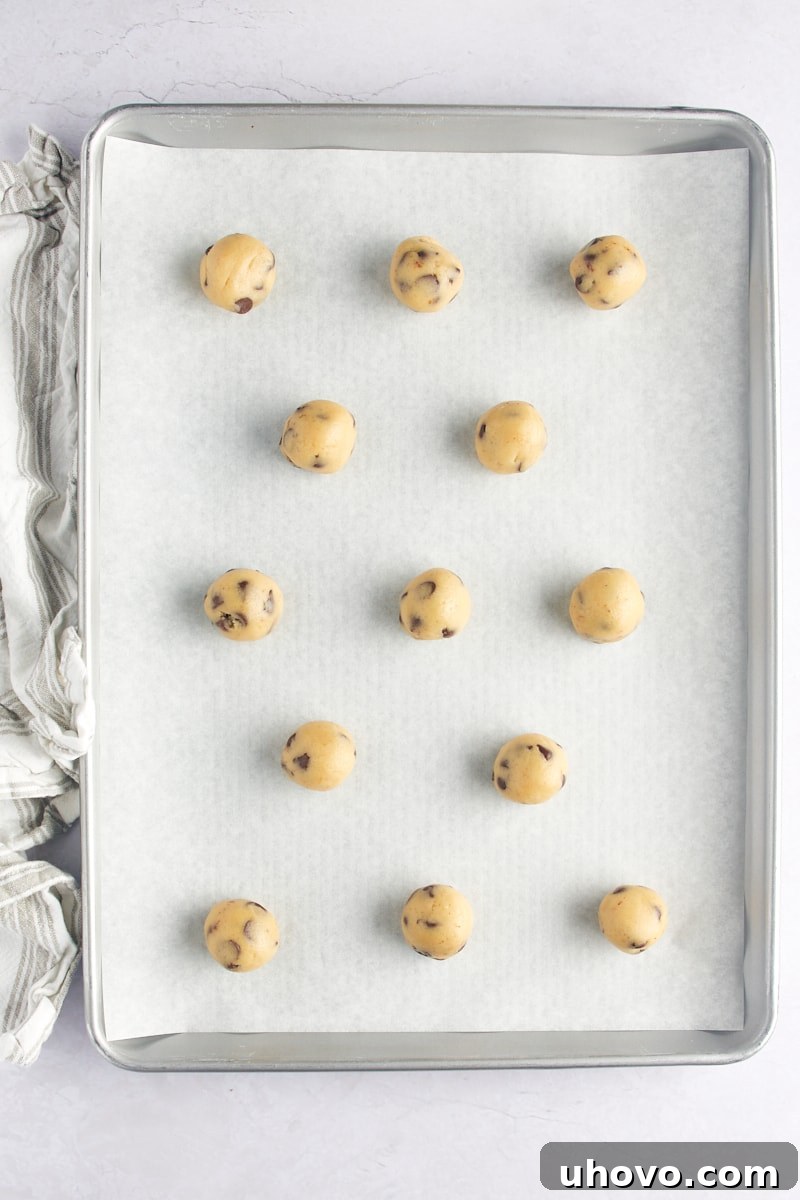 Perfectly scooped and spaced balls of chocolate chip cookie dough resting on a parchment-lined baking sheet, awaiting baking.