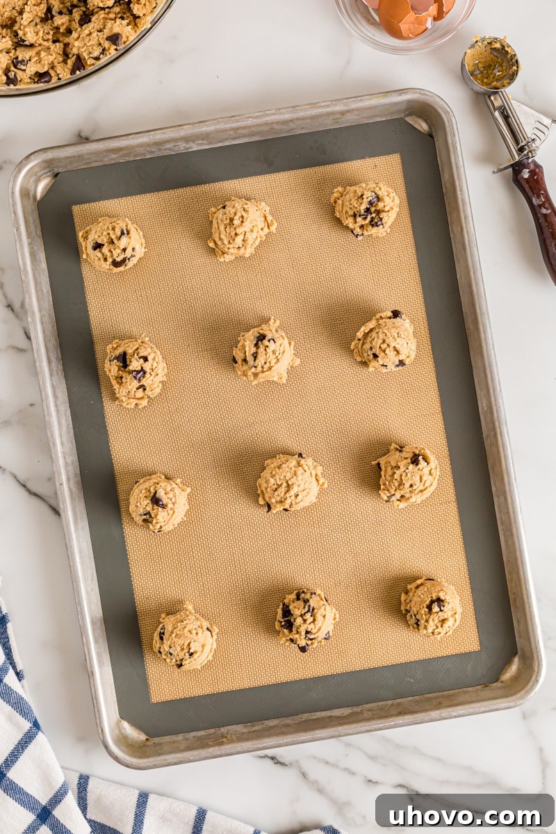 An overhead shot of uniformed oatmeal peanut butter chocolate chip cookie dough balls neatly arranged on a baking sheet, ready for the oven, awaiting their transformation.