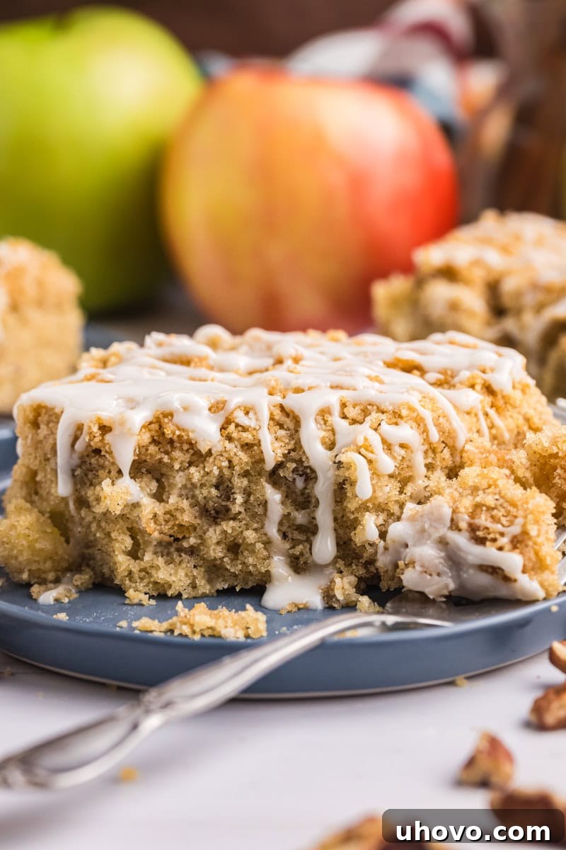 A close-up shot of a slice of apple crumb sheet cake on a white plate, with a small, inviting bite taken out and resting on a fork, beautifully showcasing the tender interior and the crisp crumb topping.