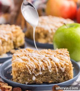 A slice of apple crumb sheet cake on a plate with glaze being drizzled over the top, showcasing the attractive final presentation of the dessert.