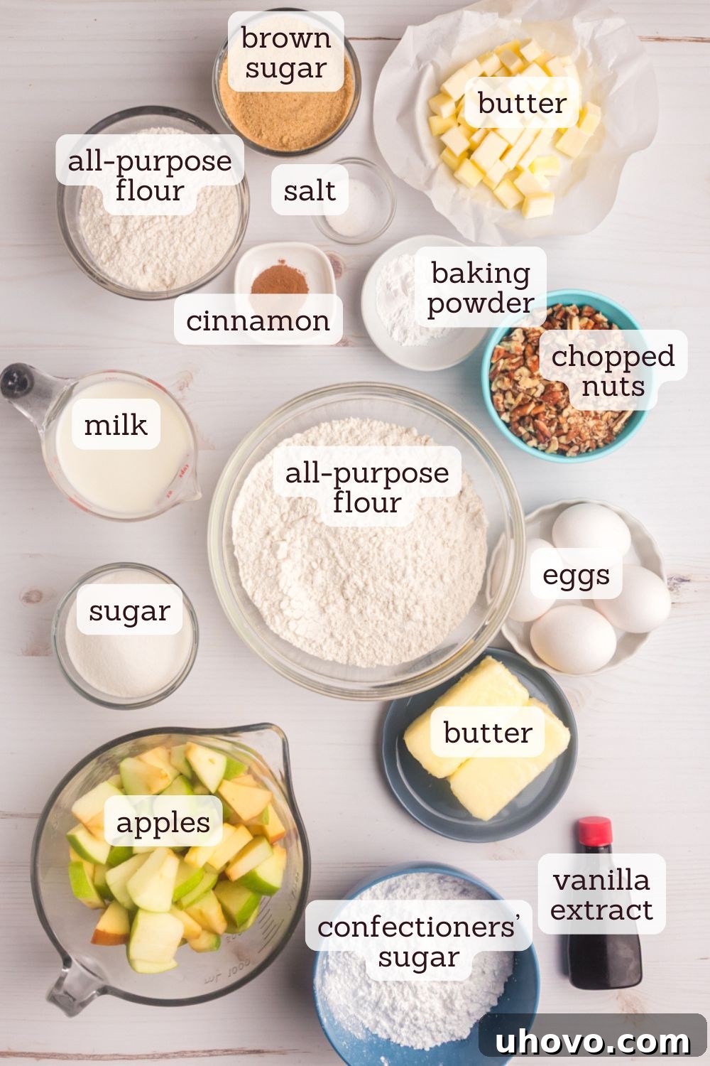 An overhead view showcasing the essential ingredients for making an apple crumb sheet cake, neatly arranged on a light surface. Ingredients include whole apples, cinnamon sticks, butter, brown sugar, granulated sugar, and dry baking components.