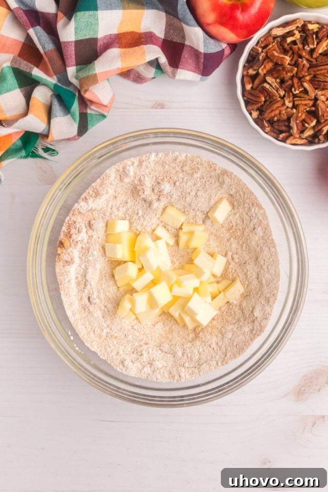 Overhead view of cold, cubed butter being added to a bowl containing flour, brown sugar, cinnamon, and salt for the crumb topping mixture.