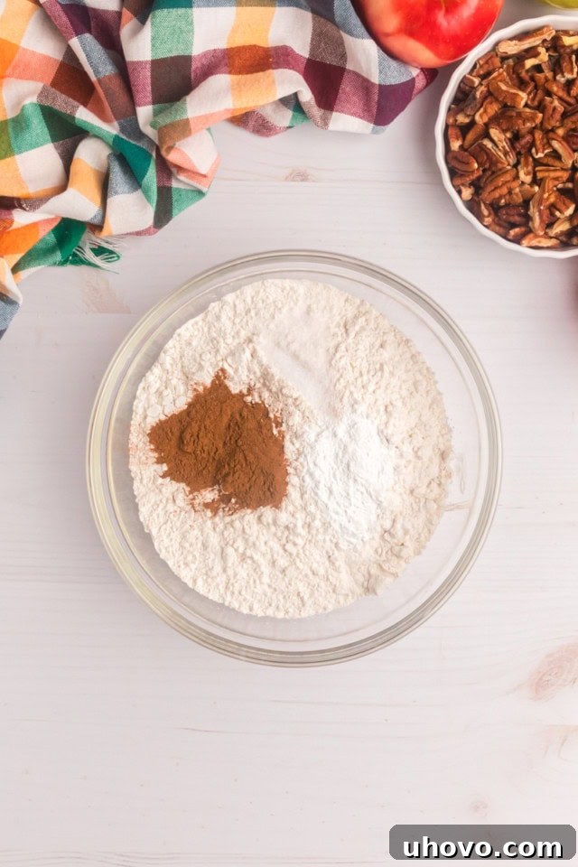 Overhead view of flour, baking powder, cinnamon, and salt meticulously mixed together in a glass mixing bowl, creating the dry component for the cake batter.