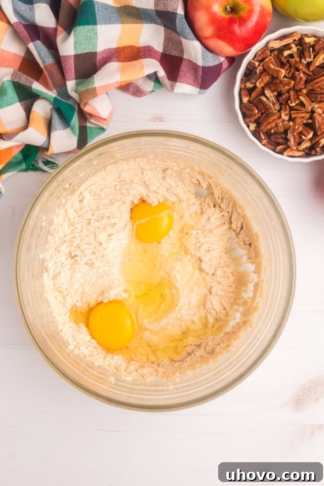 Overhead view of large eggs being carefully added to a bowl of creamed butter and sugar, ready to be beaten into a smooth, emulsified mixture.
