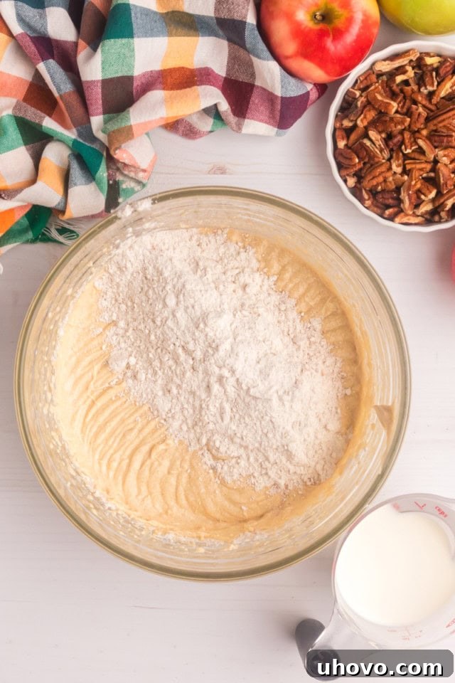Overhead view of the dry cake ingredients being gradually added to the wet cake batter in a mixing bowl, alternating with additions of milk.