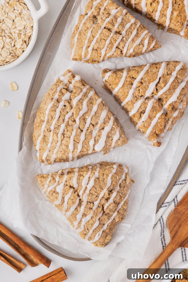 Two freshly baked cinnamon oat scones glazed and arranged on a white serving plate, with more scones blurred in the background.