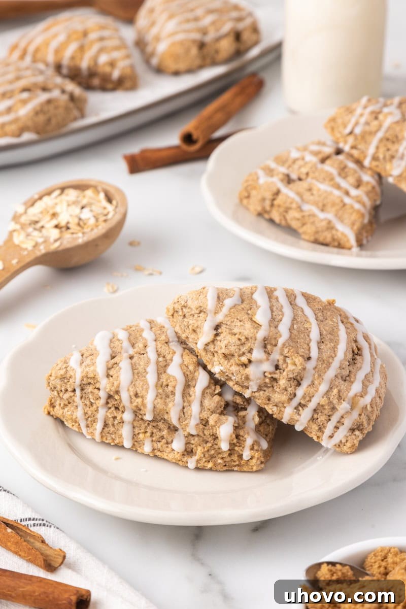 Two golden-brown cinnamon oat scones on a white plate, with more scones blurred in the background, ready to be enjoyed.
