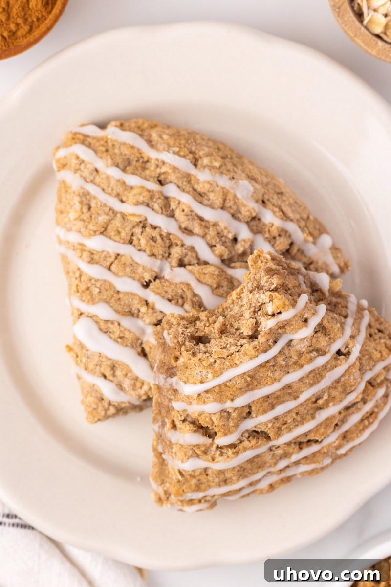 Two cinnamon oat scones on a white plate, one with a bite taken out to show the tender, fluffy interior.