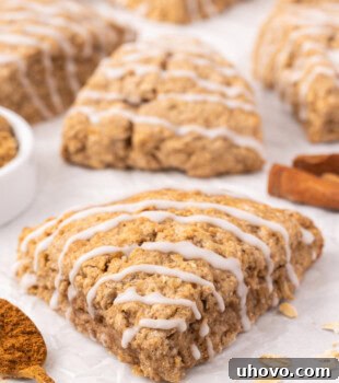 A perfectly golden-brown cinnamon oat scone on parchment paper with more scones in the background, ready to be enjoyed.