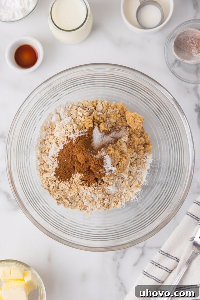 Overhead view of a glass mixing bowl filled with flour, brown sugar, oats, baking powder, baking soda, salt, and cinnamon, perfectly combined.