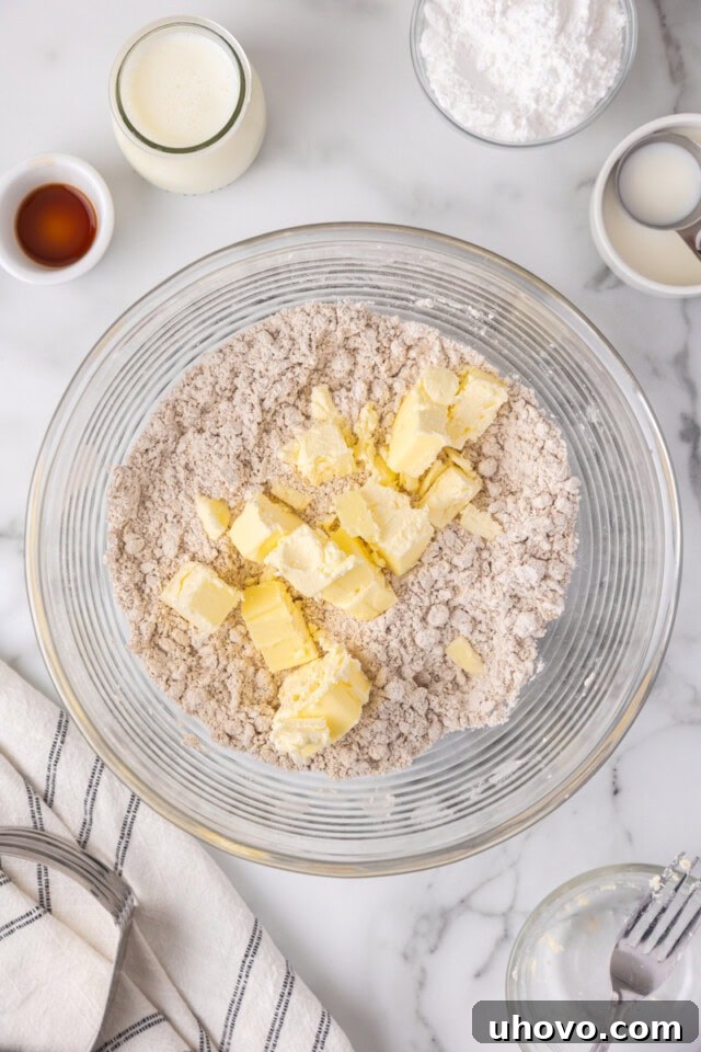 Overhead view showing cold butter cubes being added to the mixed dry ingredients in a bowl, ready to be cut in for scone dough.