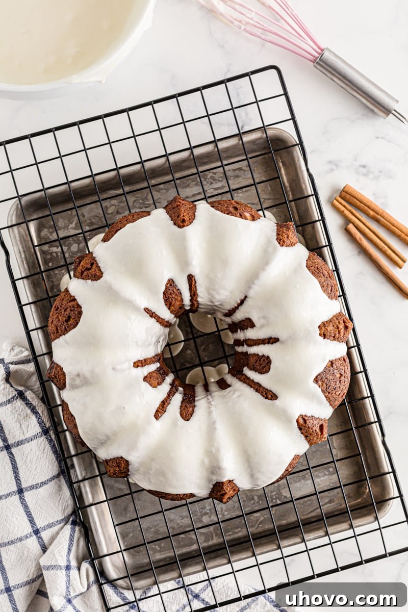 A freshly glazed Cinnamon Roll Cake set on a wire cooling rack over parchment paper