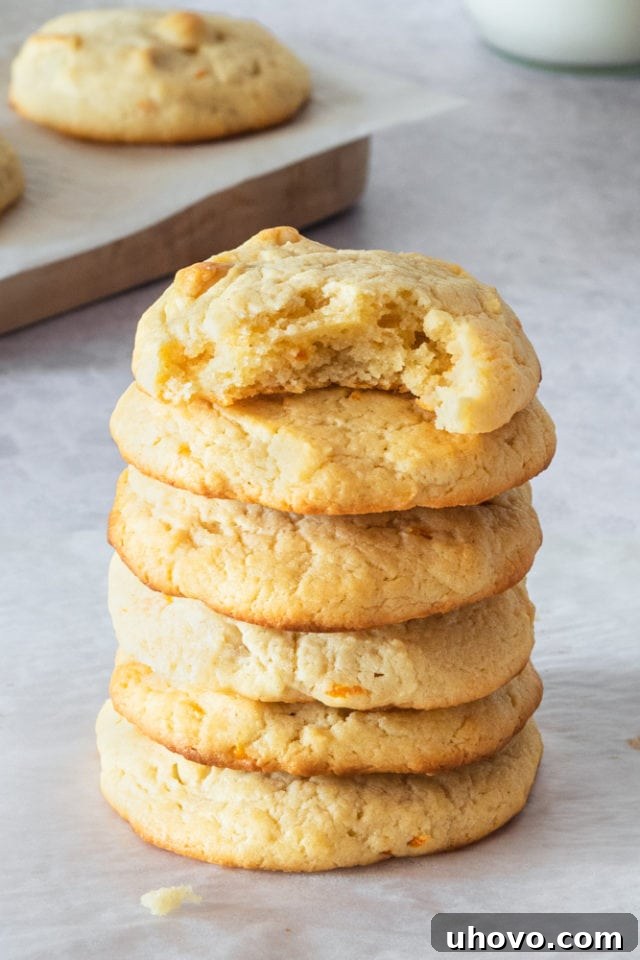 An enticing stack of perfectly baked, golden-brown Cream Cheese Macadamia Cookies resting elegantly on a minimalist gray serving surface, glistening and ready to be savored.