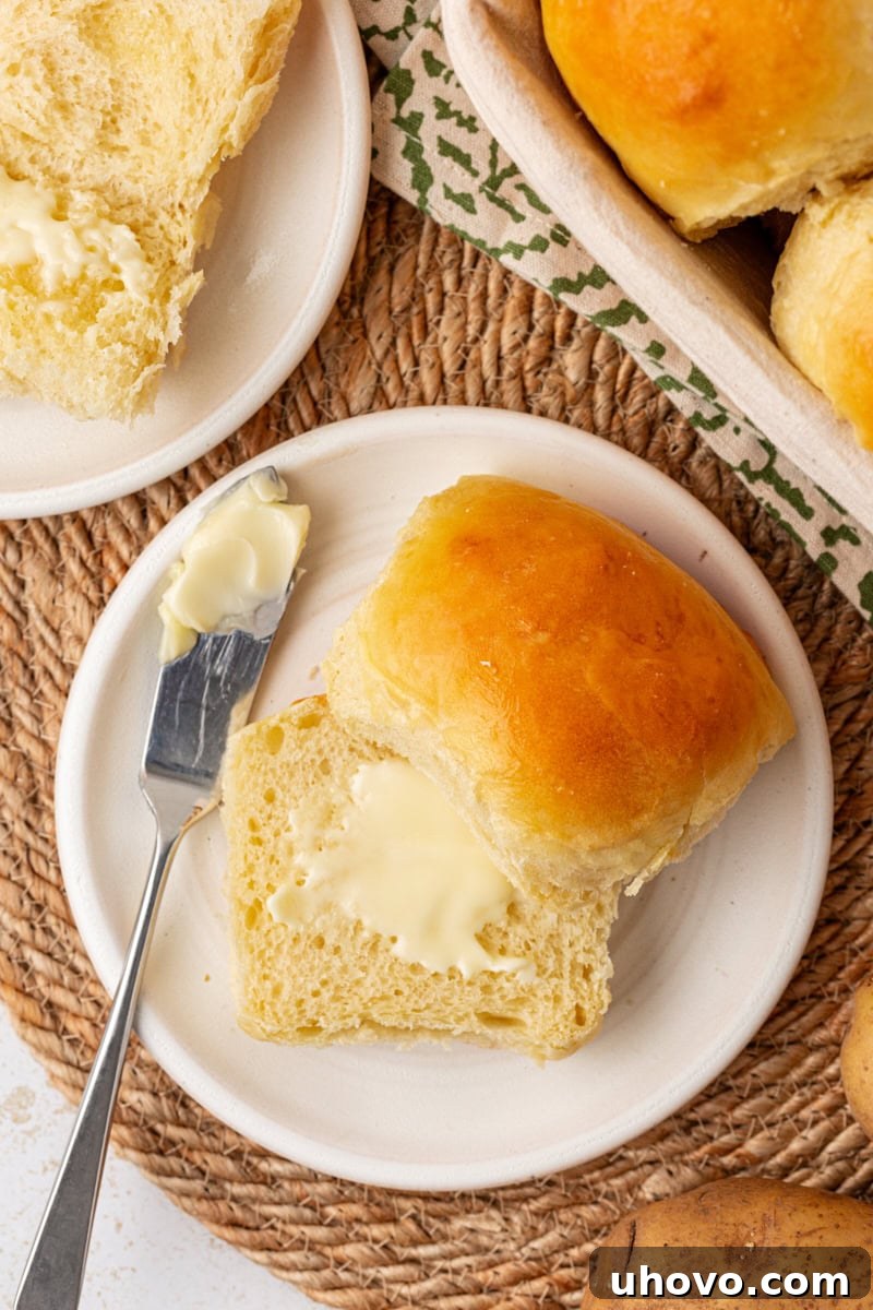 An overhead view of a single potato roll split in half, with a generous spread of butter melting into its soft, fluffy interior.