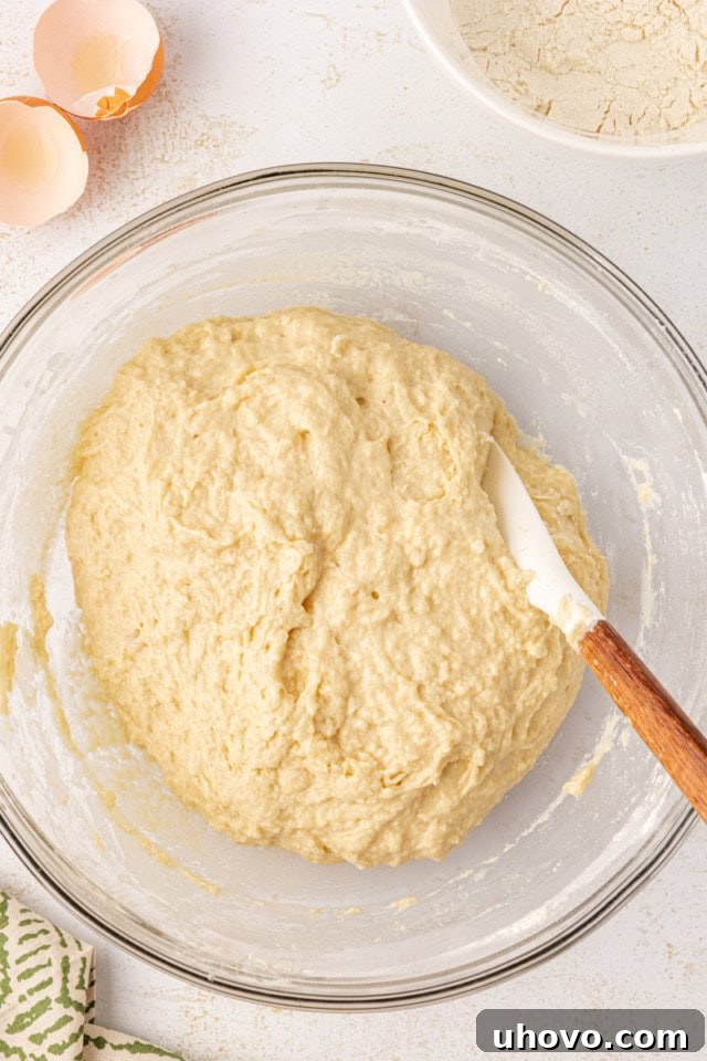An overhead view of potato roll dough in a glass mixing bowl, after the remaining flour, mashed potatoes, and eggs have been incorporated, forming a cohesive mass.