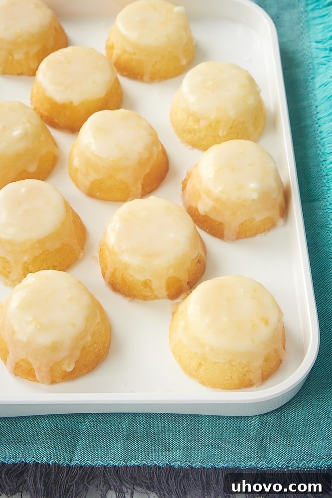 A charming close-up of Mini Lemon Pound Cakes artfully arranged on a white tray, set against a vibrant turquoise tablecloth, highlighting their irresistible texture.