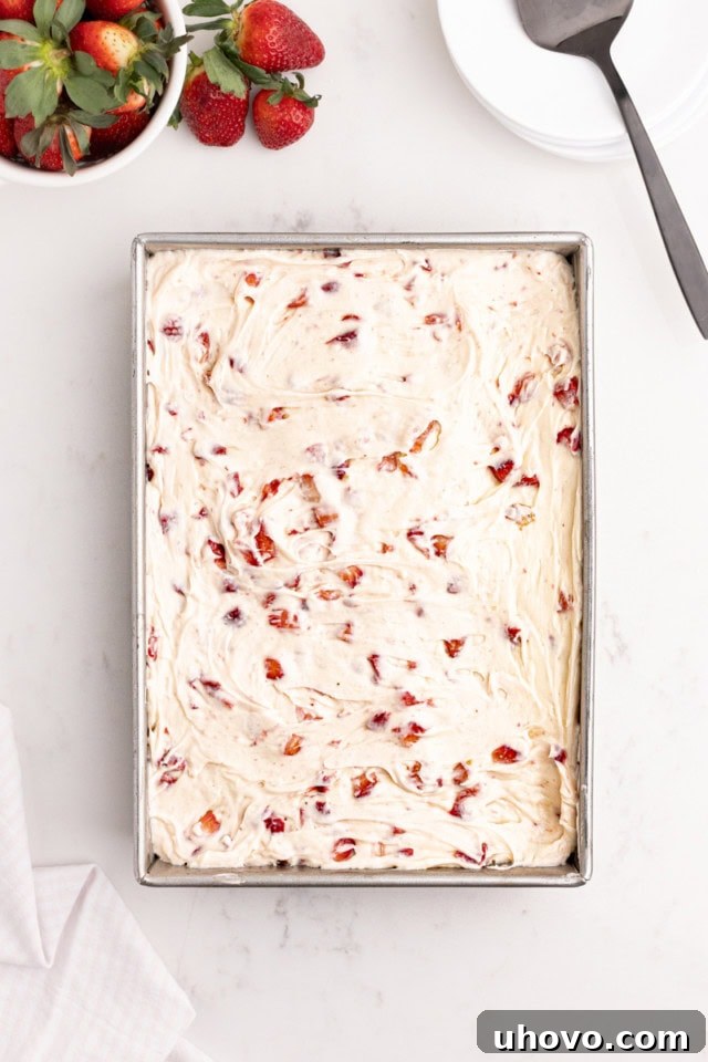A beautifully frosted strawberry sheet cake, adorned with its creamy pink frosting, presented neatly in a rectangular baking pan, signifying its readiness for serving.
